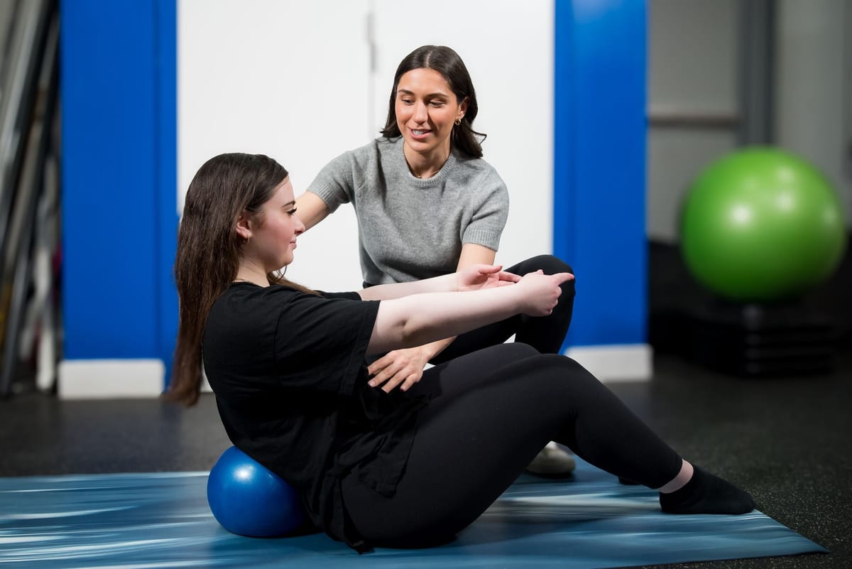 A therapist coaching a client through a core exercise on the mat