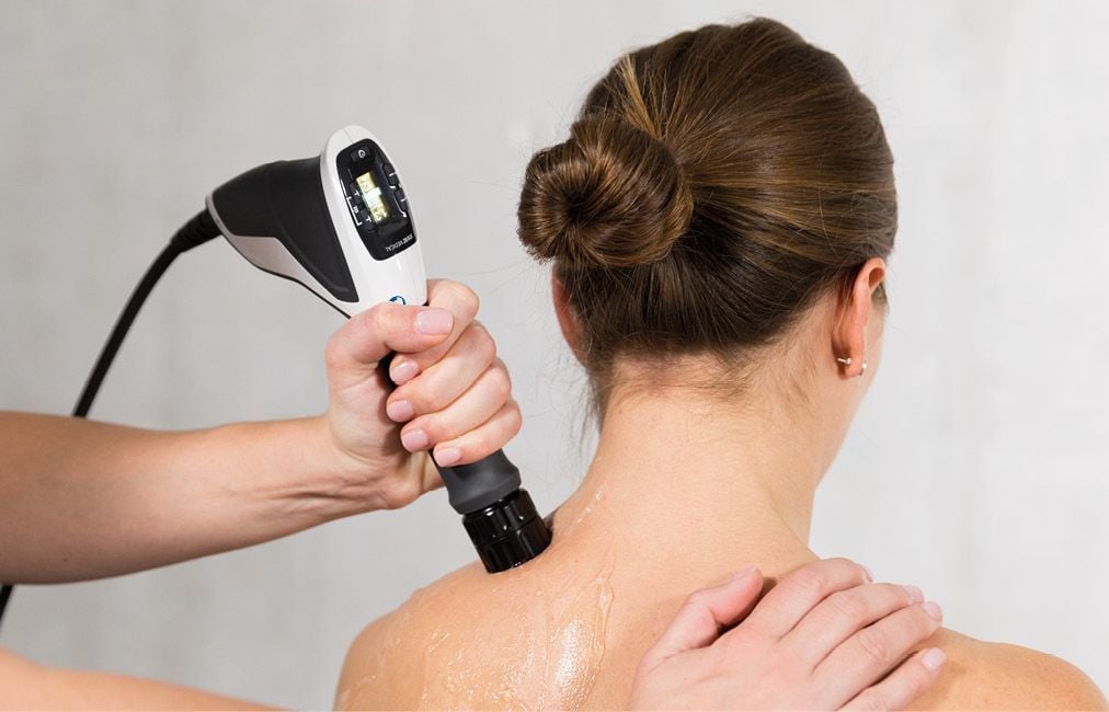 A therapist applying the shockwave therapy handpiece to a patient's shoulder